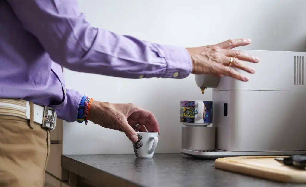 Hand stellt eine kleine Tasse unter eine Kaffeemaschine auf der Küchenarbeitsfläche