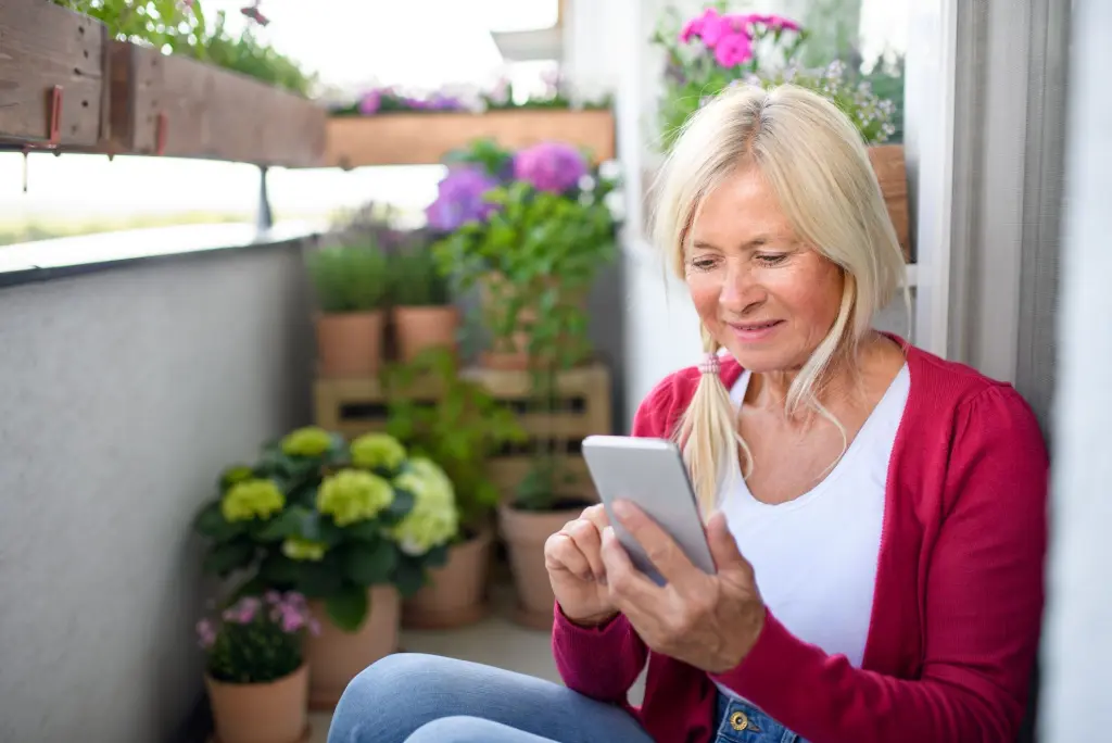 Dame die ihr Handy in der Hand hat und am Balkon sitzt